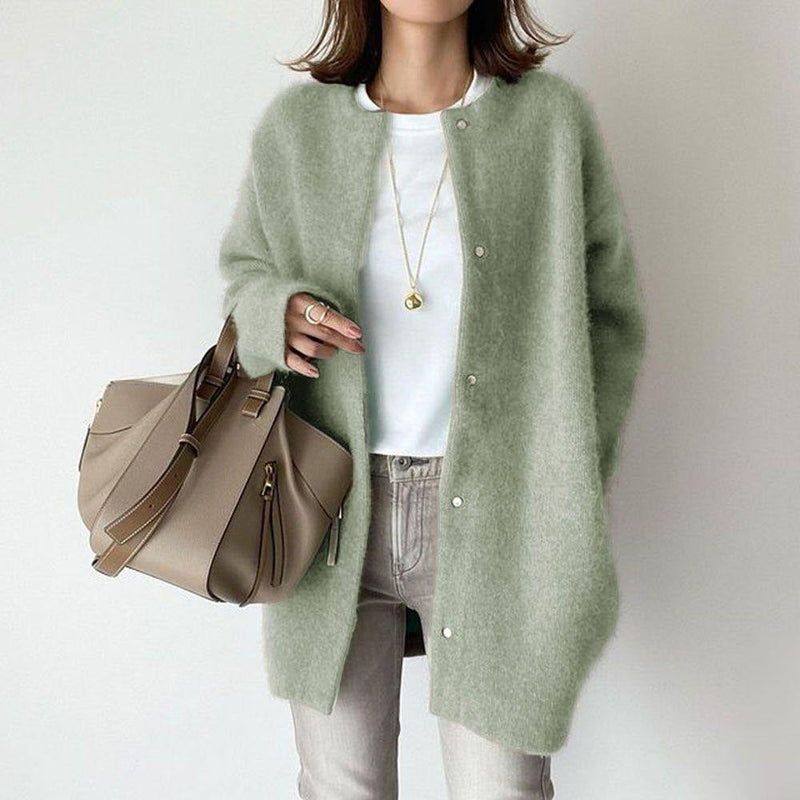 Frau in grünem Strickcardigan, weißem T-Shirt und grauer Hose, hält beige Handtasche. Modetrend, Herbstmode, Damenbekleidung, lässiger Stil.