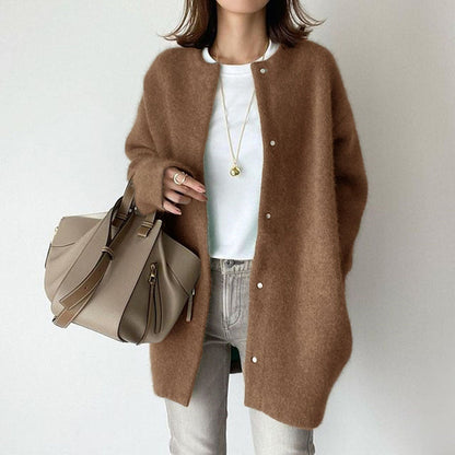 Frau in braunem Strickmantel, weißem T-Shirt und Jeans, trägt beige Handtasche. Modischer Herbst-Look, lässig und elegant.