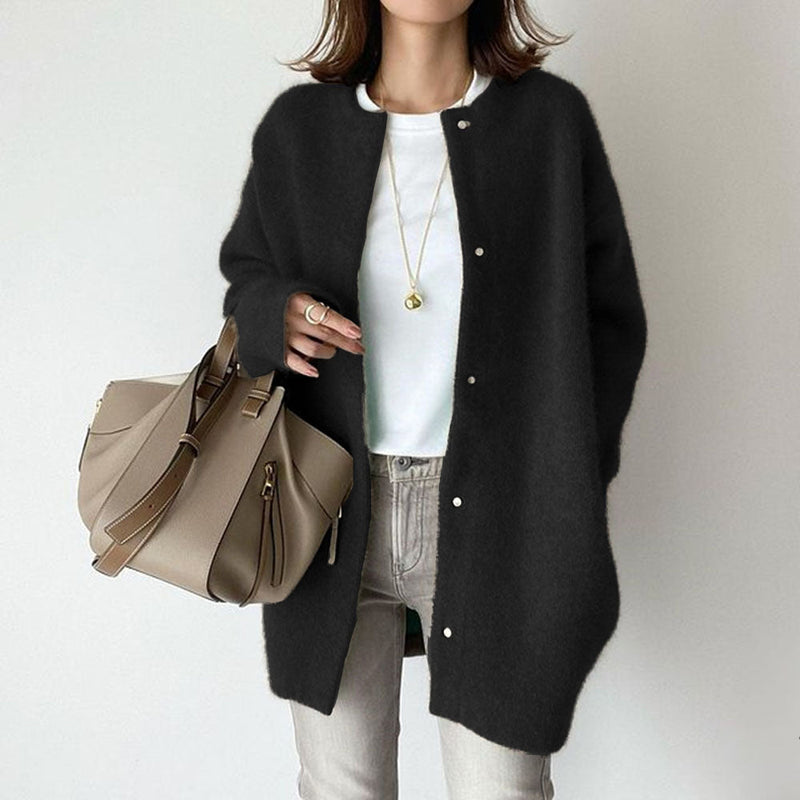 Frau in schwarzem Cardigan, weißem T-Shirt und grauer Hose, hält beige Handtasche. Modischer Herbst-Look, lässiger Stil, Damenmode.