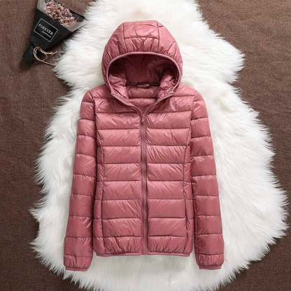 Rosa Damen-Daunenjacke mit Kapuze auf weißem Fellteppich, modische Winterbekleidung, warm und stilvoll, ideal für kalte Temperaturen.