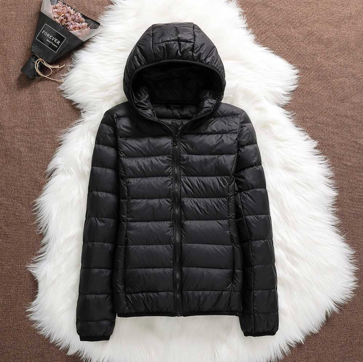 Schwarze Daunenjacke mit Kapuze auf weißem Fellteppich, modisch und warm, ideal für Winterkleidung. Perfekt für Outdoor-Aktivitäten.