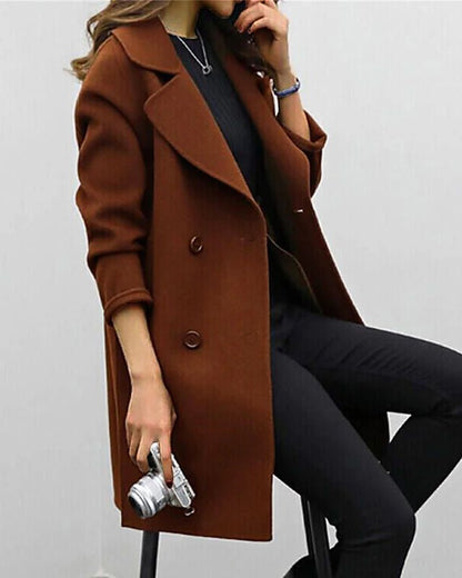 Frau in braunem Wollmantel, hält Kamera, sitzt auf Hocker. Stilvolle Herbstmode, eleganter Look, Damenbekleidung, Fotografie-Accessoire.