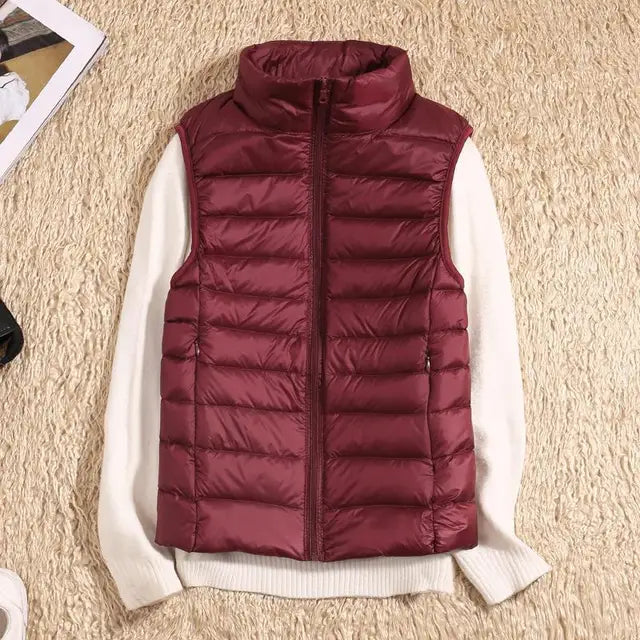 Bordeauxrote Daunenweste auf cremefarbenem Pullover, flach auf beigem Teppich. Modetrend, Herbstbekleidung, warme Oberbekleidung.