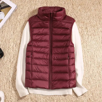 Bordeauxrote Daunenweste auf cremefarbenem Pullover, flach auf beigem Teppich. Modetrend, Herbstbekleidung, warme Oberbekleidung.