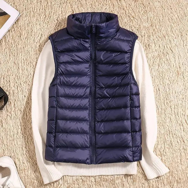 Dunkelblaue Steppweste auf weißem Pullover, beige Teppich. Modische Winterbekleidung, ärmellose Jacke, warme Outdoor-Weste.