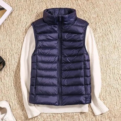 Dunkelblaue Steppweste auf weißem Pullover, beige Teppich. Modische Winterbekleidung, ärmellose Jacke, warme Outdoor-Weste.