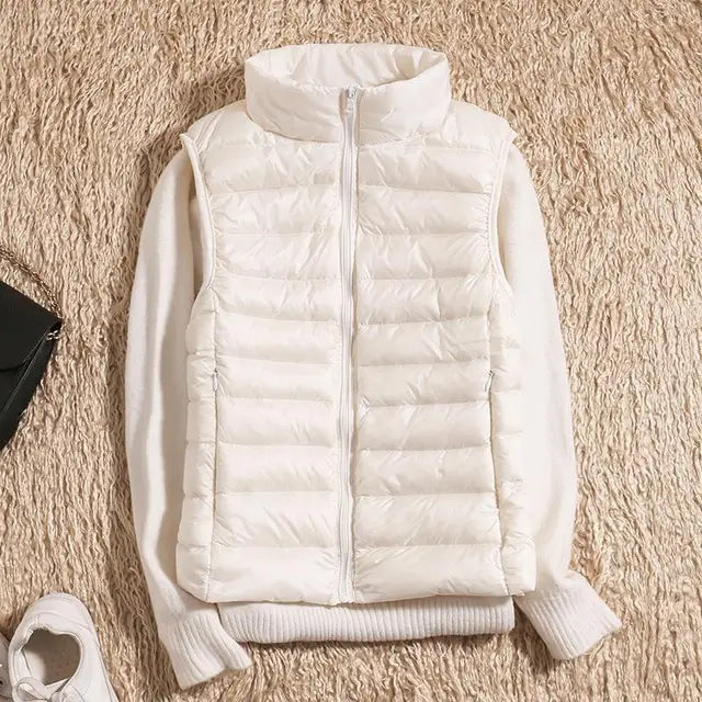 Weiße Daunenweste auf beigem Teppich, kombiniert mit weißem Pullover. Modetrend, Winterbekleidung, stilvolle Damenmode, warme Oberbekleidung.