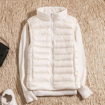 Weiße Daunenweste auf beigem Teppich, kombiniert mit weißem Pullover. Modetrend, Winterbekleidung, stilvolle Damenmode, warme Oberbekleidung.