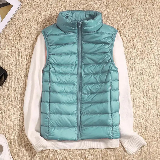Türkisfarbene Steppweste auf cremefarbenem Pullover, flach auf beigem Teppich. Modische Damenbekleidung, Herbstmode, ärmellose Jacke.