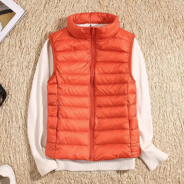 Orangefarbene Steppweste auf cremefarbenem Pullover, flach auf beigem Teppich liegend. Modetrend, Herbstbekleidung, warme Outdoor-Weste.