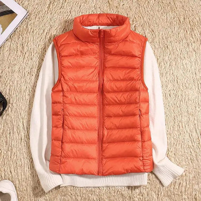 Orangefarbene Steppweste auf cremefarbenem Pullover, flach auf beigem Teppich liegend. Modetrend, Herbstbekleidung, warme Outdoor-Weste.