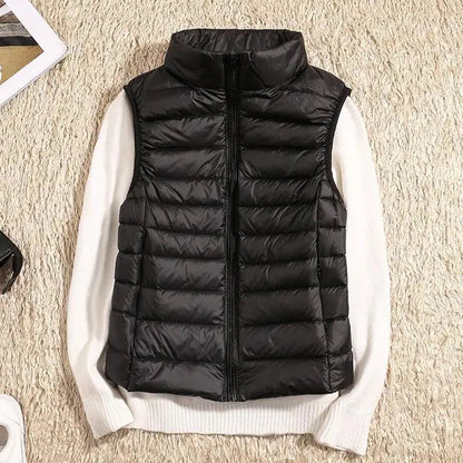Schwarze Daunenweste auf weißem Pullover, flach auf beigem Teppich. Modische Winterbekleidung, warm und stilvoll, ideal für kalte Tage.