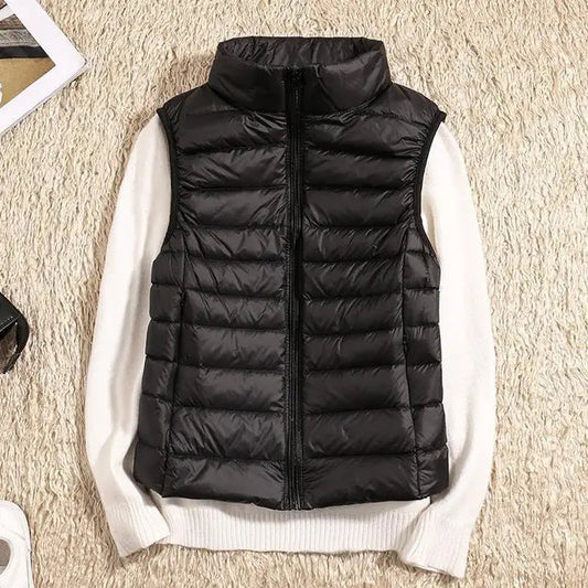 Schwarze Daunenweste auf weißem Pullover, flach auf beigem Teppich. Modische Winterbekleidung, warm und stilvoll, ideal für kalte Tage.