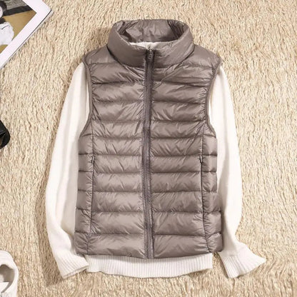 Graue Daunenweste mit Reißverschluss auf cremefarbenem Pullover, flach auf beigem Teppich liegend. Modetrend, Herbstbekleidung, Damenmode.