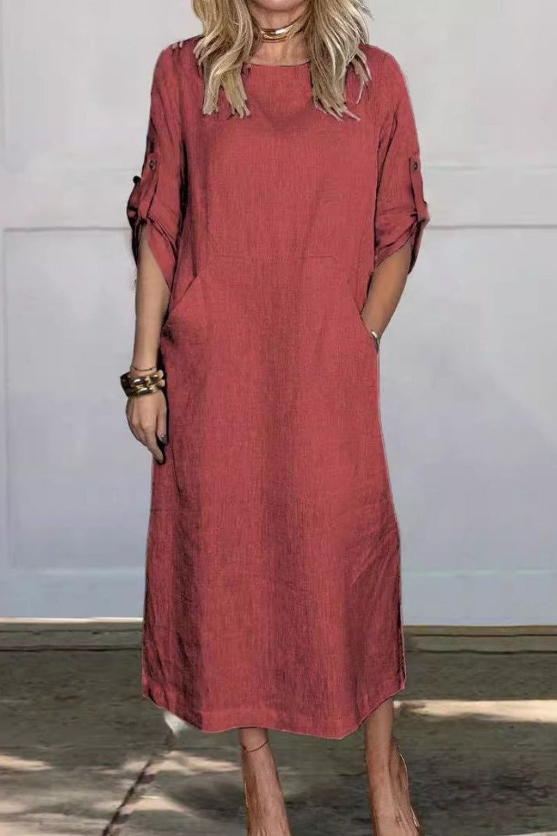 Frau in rotem Leinenkleid mit hochgekrempelten Ärmeln, stehend vor grauer Wand. Modetrend, lässiger Stil, Sommerkleidung, Damenmode.