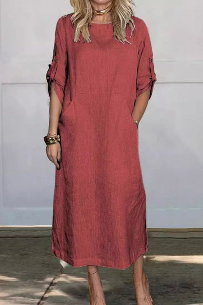 Frau in rotem Leinenkleid mit hochgekrempelten Ärmeln, stehend vor grauer Wand. Modetrend, lässiger Stil, Sommerkleidung, Damenmode.