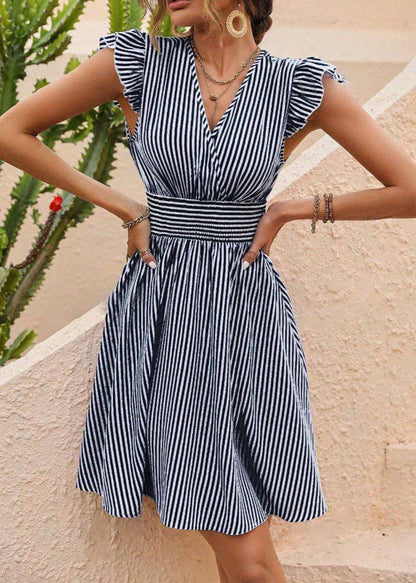 Frau in gestreiftem Sommerkleid mit V-Ausschnitt und Rüschenärmeln, steht vor einer Wand mit Kaktus im Hintergrund. Modetrend, Damenmode, Sommerkleid.