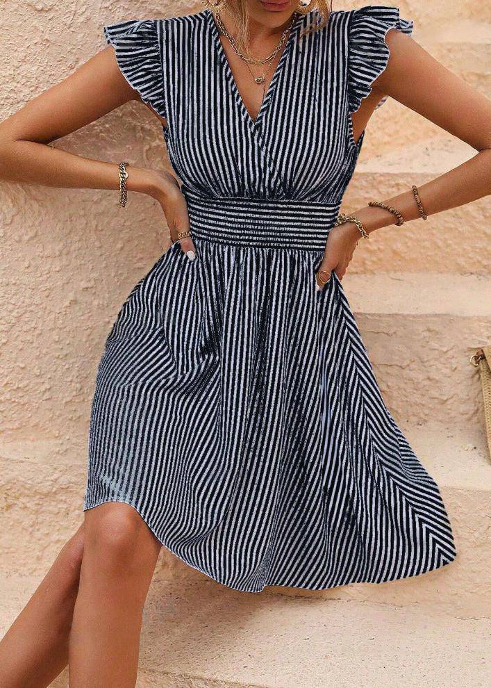 Frau in gestreiftem Sommerkleid mit Rüschenärmeln sitzt auf Treppe. Modisches Damenkleid, blau-weiß gestreift, ideal für Sommermode.