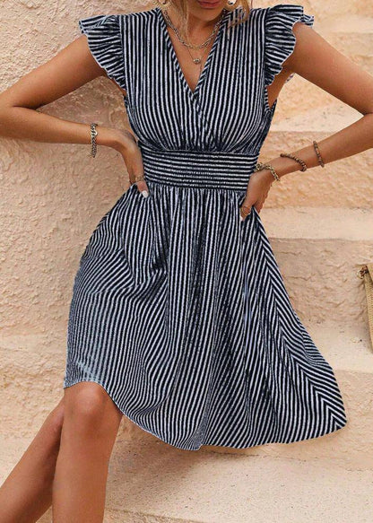 Frau in gestreiftem Sommerkleid mit Rüschenärmeln sitzt auf Treppe. Modisches Damenkleid, blau-weiß gestreift, ideal für Sommermode.