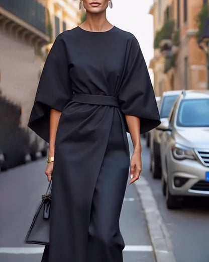 Elegante Frau in schwarzem Kleid mit weitem Schnitt und Gürtel, trägt schwarze Handtasche, läuft auf städtischer Straße, Mode, Streetstyle.