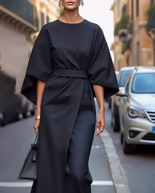 Elegante Frau in schwarzem Kleid mit weitem Schnitt und Gürtel, trägt schwarze Handtasche, läuft auf städtischer Straße, Mode, Streetstyle.