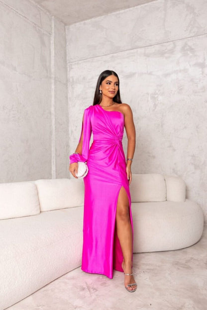 Frau in einem leuchtend pinken, schulterfreien Abendkleid mit hohem Beinschlitz, steht vor einer modernen, minimalistischen Betonwand.