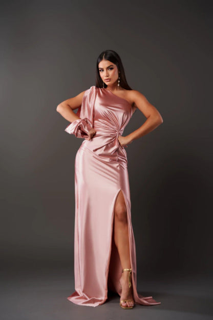 Frau in eleganter, rosafarbener Abendkleid mit asymmetrischem Schnitt und hohem Beinschlitz, posiert vor grauem Hintergrund. Mode, Abendgarderobe.