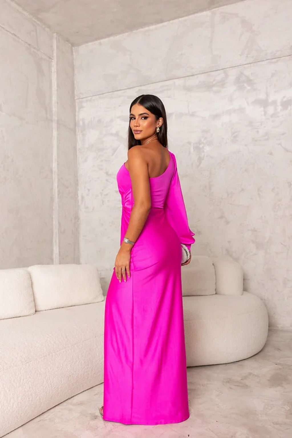 Frau in einem leuchtend pinken, schulterfreien Abendkleid posiert vor einer modernen, minimalistischen Couch in einem stilvollen Raum.