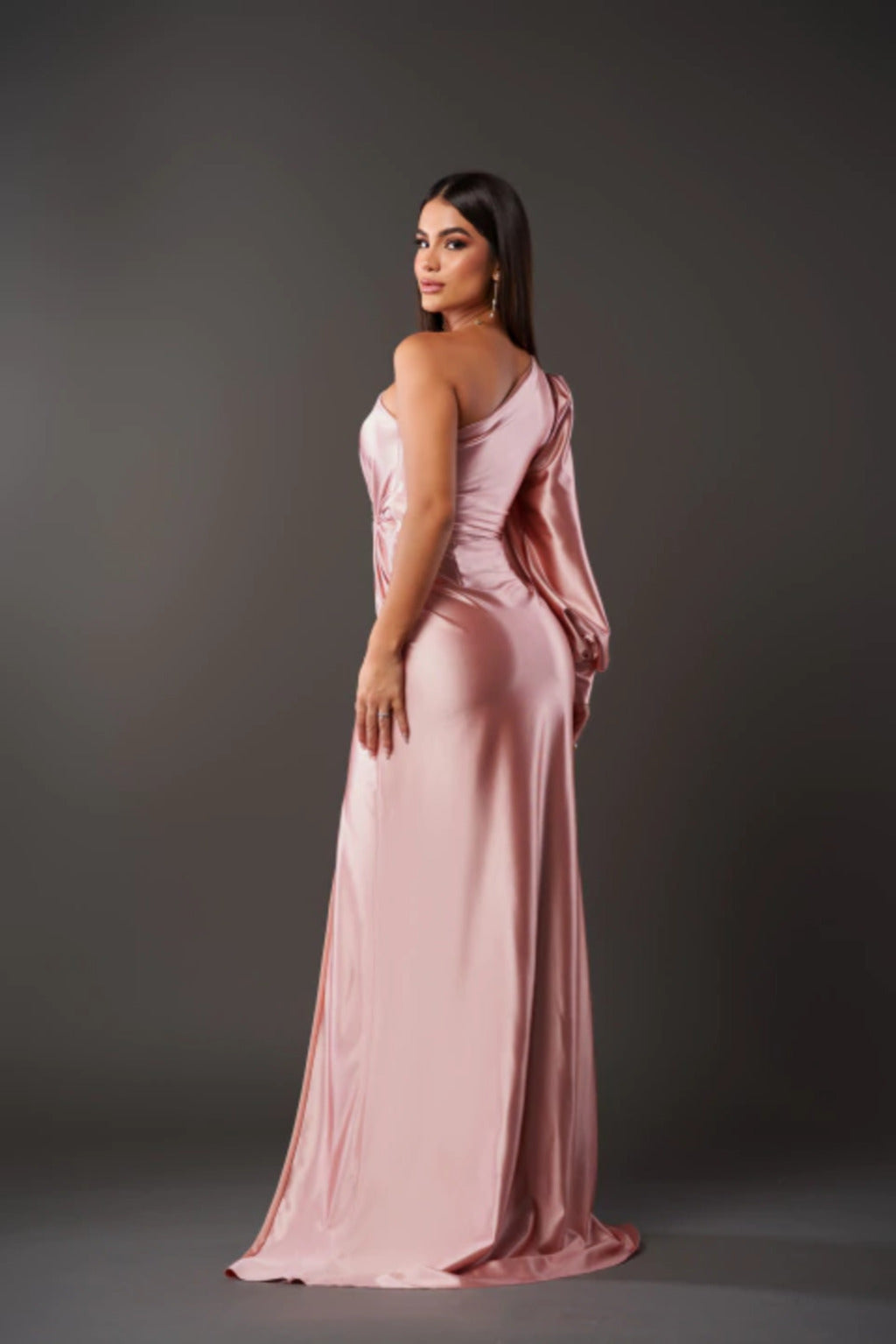 Frau in elegantem, rosa Abendkleid mit asymmetrischem Schnitt, posiert vor grauem Hintergrund. Mode, Abendgarderobe, stilvolles Design.