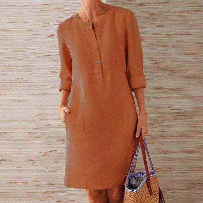 Braunes Leinenkleid mit Knopfleiste und Taschen, getragen von einer Person, die eine gestreifte Strohtasche hält. Ideal für Sommermode und Freizeit.