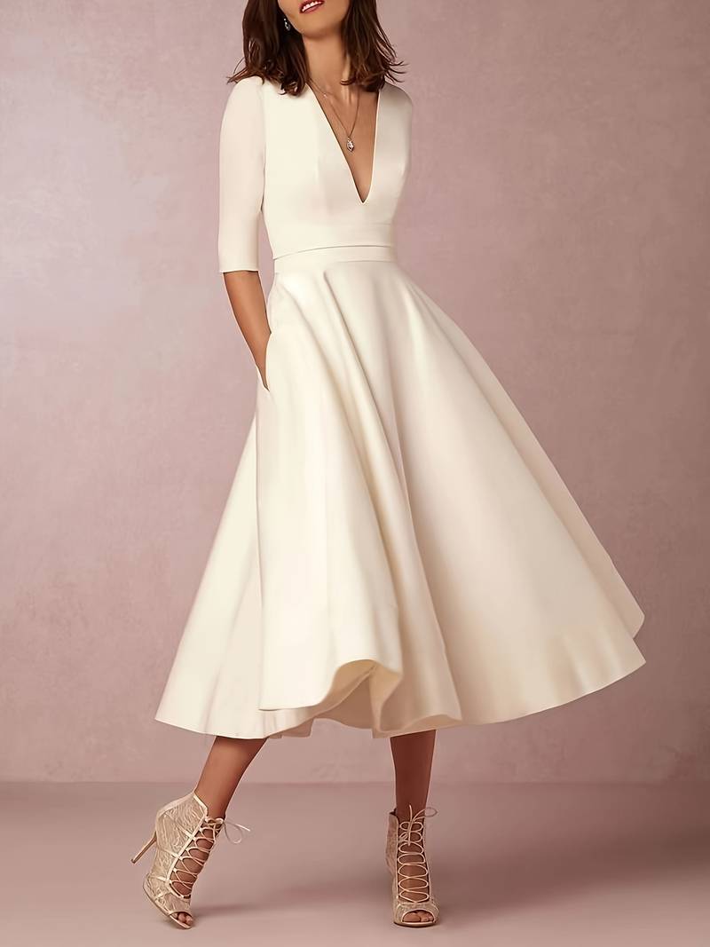 Frau in elegantem cremefarbenem Kleid mit V-Ausschnitt und halblangen Ärmeln, kombiniert mit Spitzen-High-Heels. Perfekt für Hochzeiten oder formelle Anlässe.