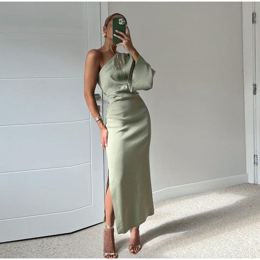 Frau in elegantem, einarmigem, olivgrünem Kleid mit hohem Schlitz posiert vor weißer Tür. Mode, Abendkleid, stilvoll, modern.