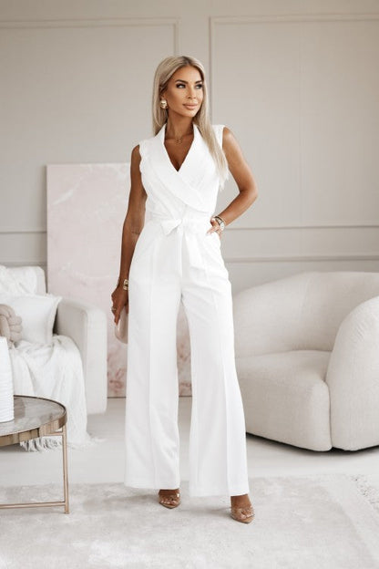 Frau in elegantem weißen Jumpsuit steht in modernem Wohnzimmer. Stilvolle Mode, schickes Design, luxuriöse Inneneinrichtung, zeitgenössischer Look.