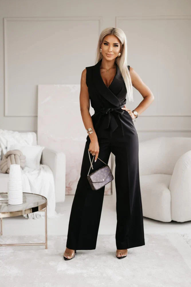 Elegante Frau in schwarzem Jumpsuit posiert in modernem Wohnzimmer, hält eine Designer-Handtasche. Stilvolle Mode, luxuriöse Inneneinrichtung.