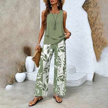 Frau in grünem ärmellosen Top und weiß-grüner Blattmusterhose, Strohhut, Sandalen, mit Clutch, vor rustikalem Hintergrund. Sommermode, Boho-Stil.