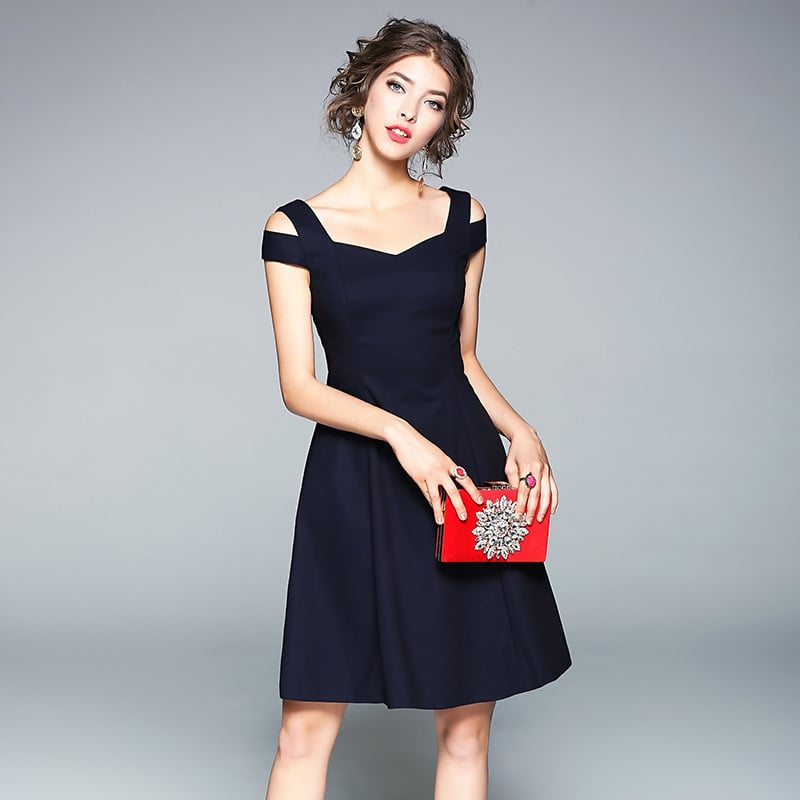 Eine Frau in einem eleganten, schwarzen Cocktailkleid mit Trägern hält eine rote Clutch. Perfekt für Abendmode und stilvolle Anlässe.
