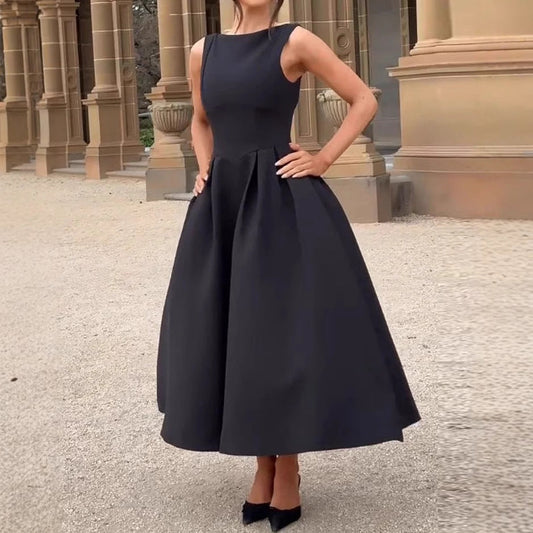 Elegantes schwarzes Abendkleid, ärmellos und knielang, getragen von einer Frau vor einem historischen Gebäude. Perfekt für formelle Anlässe.
