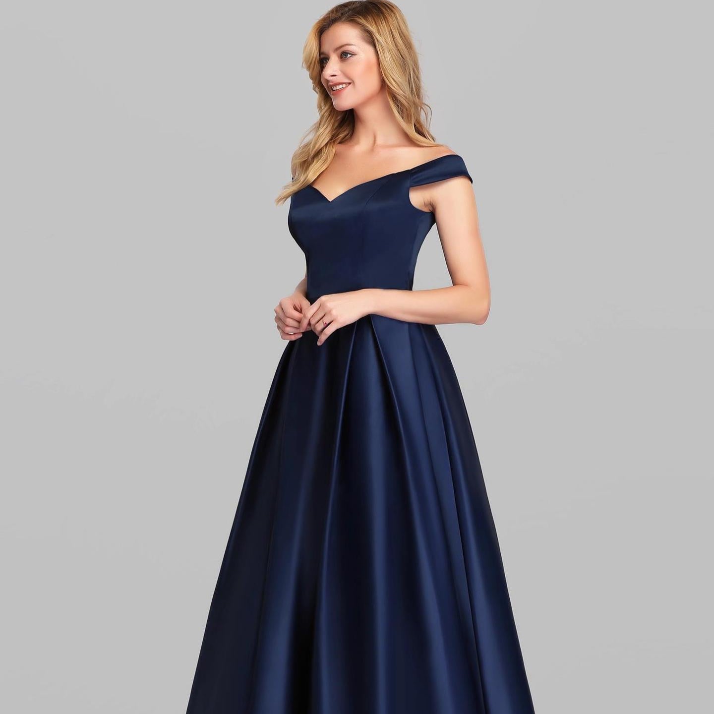 Frau in elegantem, schulterfreiem, dunkelblauem Abendkleid vor grauem Hintergrund. Perfekt für formelle Anlässe und Abendveranstaltungen.