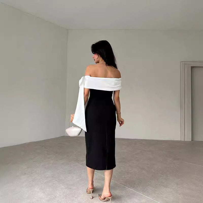 Frau in schulterfreiem, schwarzem Kleid mit weißem Schal, hält eine kleine Tasche. Elegante Mode, minimalistischer Raum, stilvolle Abendgarderobe.