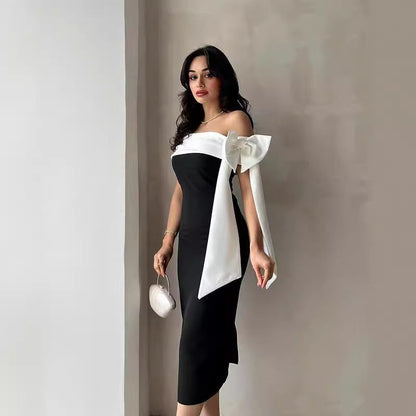 Schwarzes schulterfreies Kleid mit weißer Schleife, elegante Abendmode, Frau mit Handtasche, stilvolles Design, Modefotografie.