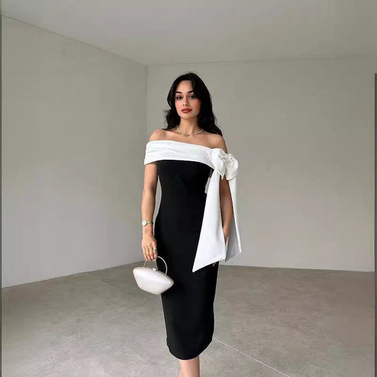 Frau in elegantem, schulterfreiem schwarzen Kleid mit weißer Schleife, hält eine kleine Handtasche. Minimalistischer Hintergrund. Mode, Abendkleid.