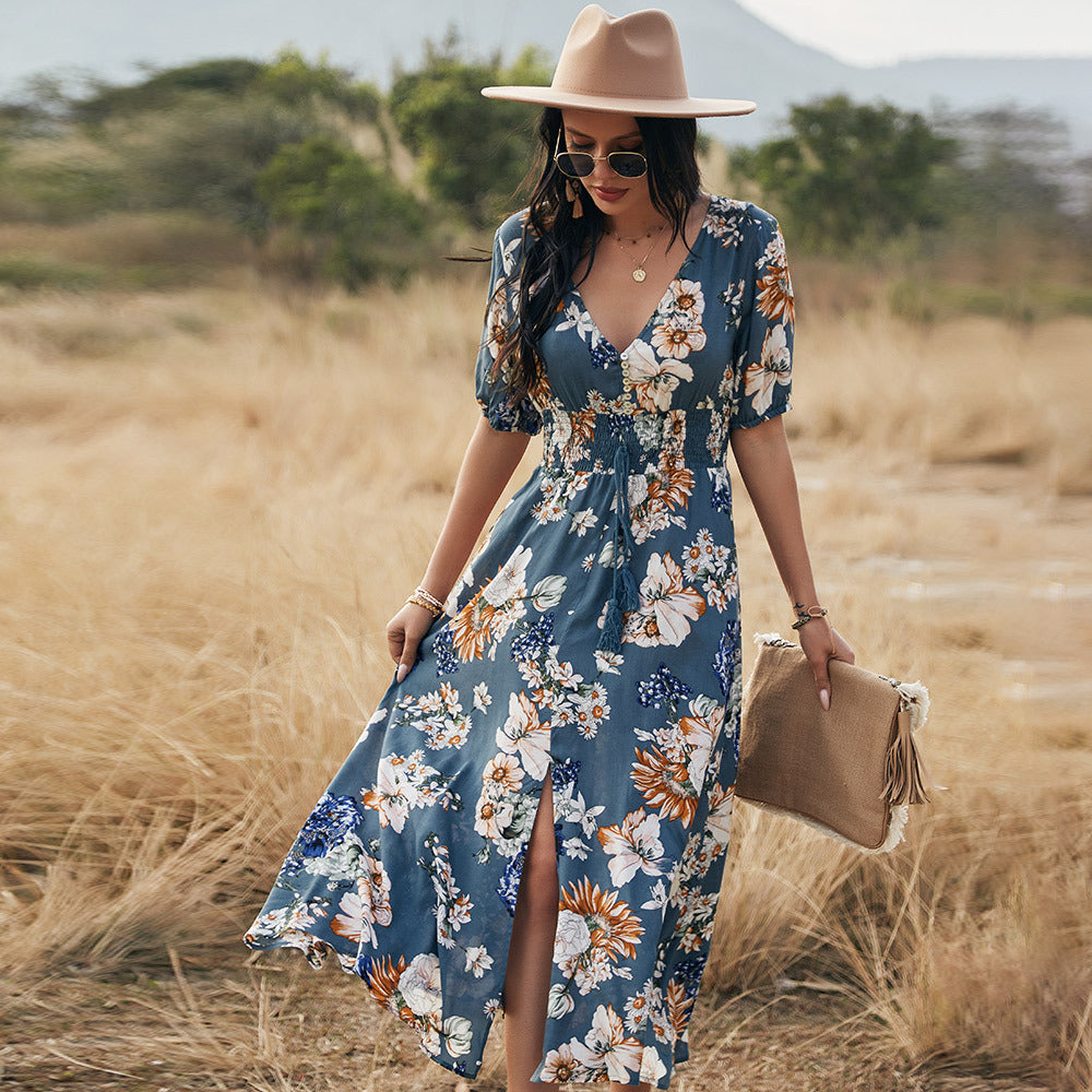 Frau in geblümtem Maxikleid und Hut spaziert durch eine Wiese. Sommermode, Boho-Stil, Freizeitkleidung, Naturhintergrund.