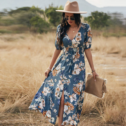 Frau in geblümtem Maxikleid und Hut spaziert durch eine Wiese. Sommermode, Boho-Stil, Freizeitkleidung, Naturhintergrund.