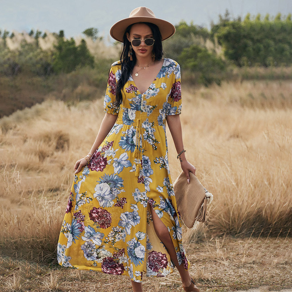Frau in gelbem, geblümtem Maxikleid und Sonnenhut steht auf einem Feld. Sommermode, Boho-Stil, Freizeitkleidung, Outdoor-Fotografie.