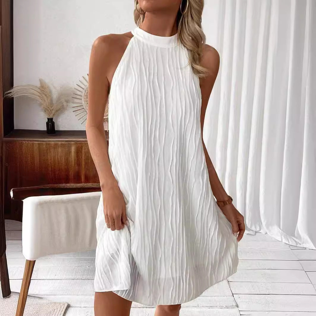 Frau in elegantem, ärmellosem weißen Kleid mit plissiertem Design, steht in modernem, minimalistischem Raum. Sommermode, Damenkleid, stilvoll.