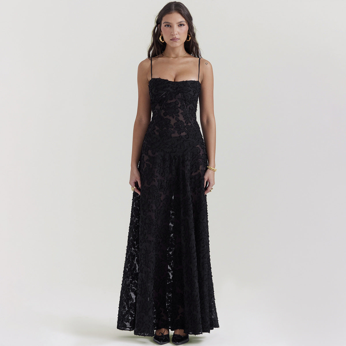 Frau in elegantem, schwarzem Abendkleid mit Spitzenmuster, Spaghettiträgern und bodenlangem Schnitt. Perfekt für formelle Anlässe und Abendveranstaltungen.
