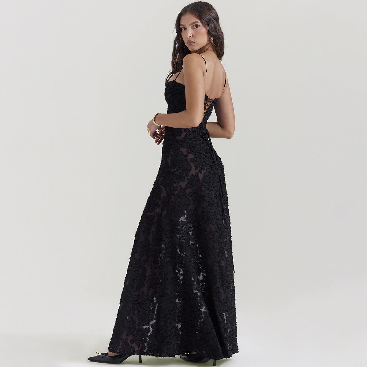 Frau in elegantem, schwarzem Abendkleid mit Spitzenmuster, seitlich stehend. Perfekt für formelle Anlässe, stilvoll und zeitlos.