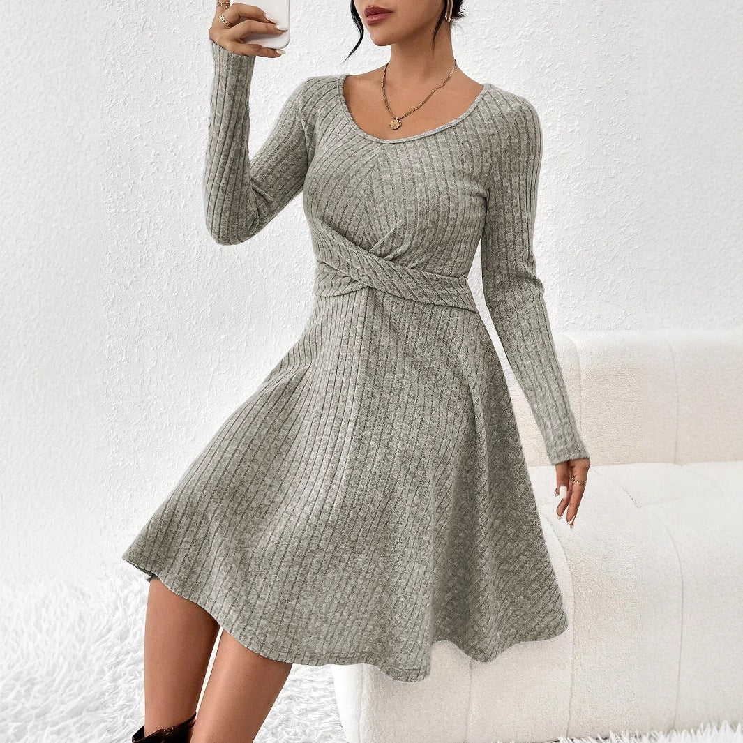 Frau in grauem Strickkleid mit langen Ärmeln, posiert vor weißem Hintergrund. Modisches Winteroutfit, elegantes Design, gemütlicher Look.