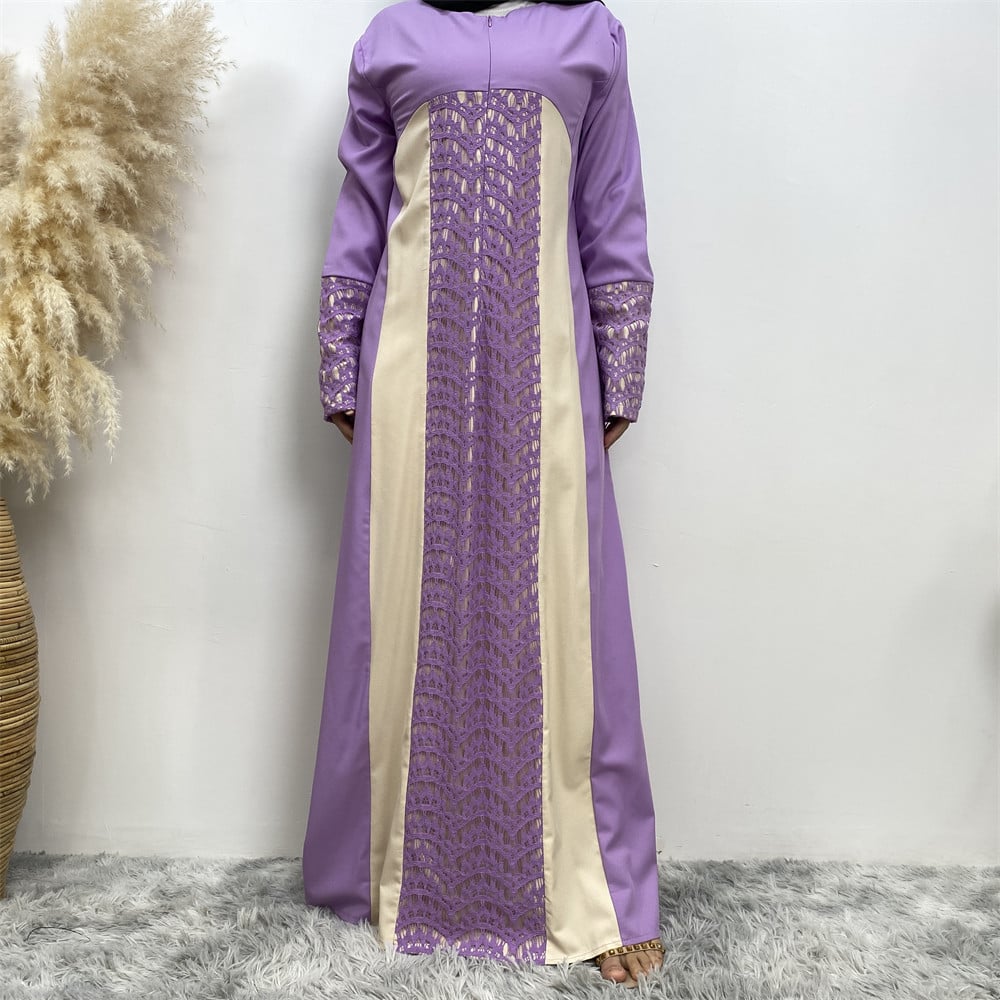 Langes lila Kleid mit beigem Einsatz und Spitzenmuster, stehend auf grauem Teppich, neben dekorativem Pampasgras in einem Korb.