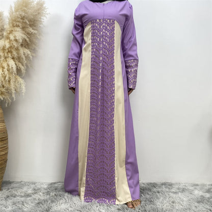 Langes lila Kleid mit beigem Einsatz und Spitzenmuster, stehend auf grauem Teppich, neben dekorativem Pampasgras in einem Korb.